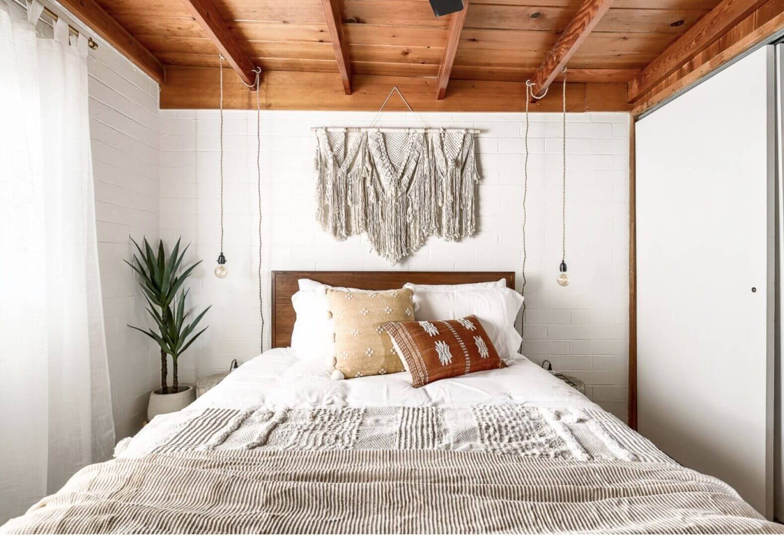Cozy boho bedroom with wooden ceiling and macrame wall hanging.