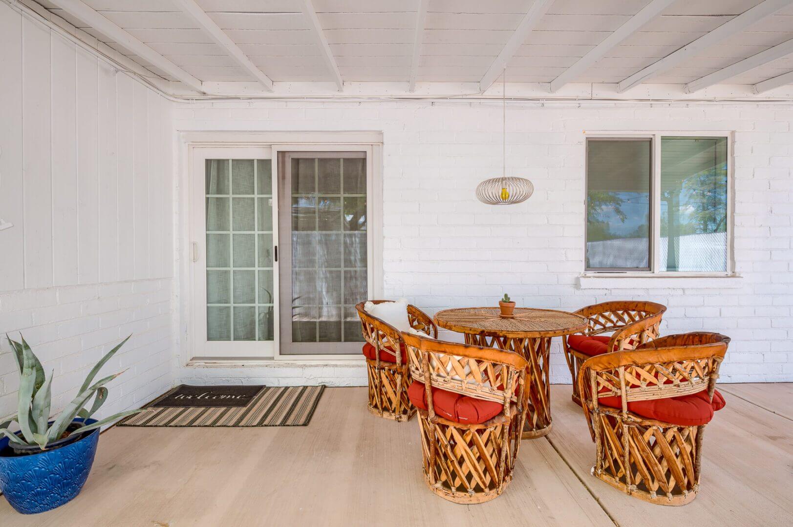 Cozy outdoor dining area with wicker chairs and a table on a covered porch.