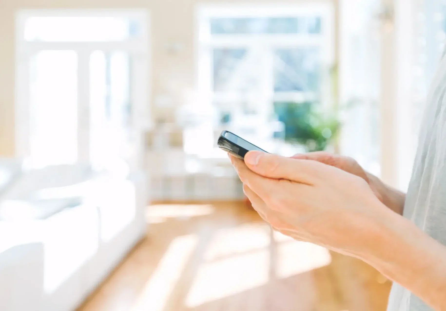 Person holding a TV remote control in a bright living room.