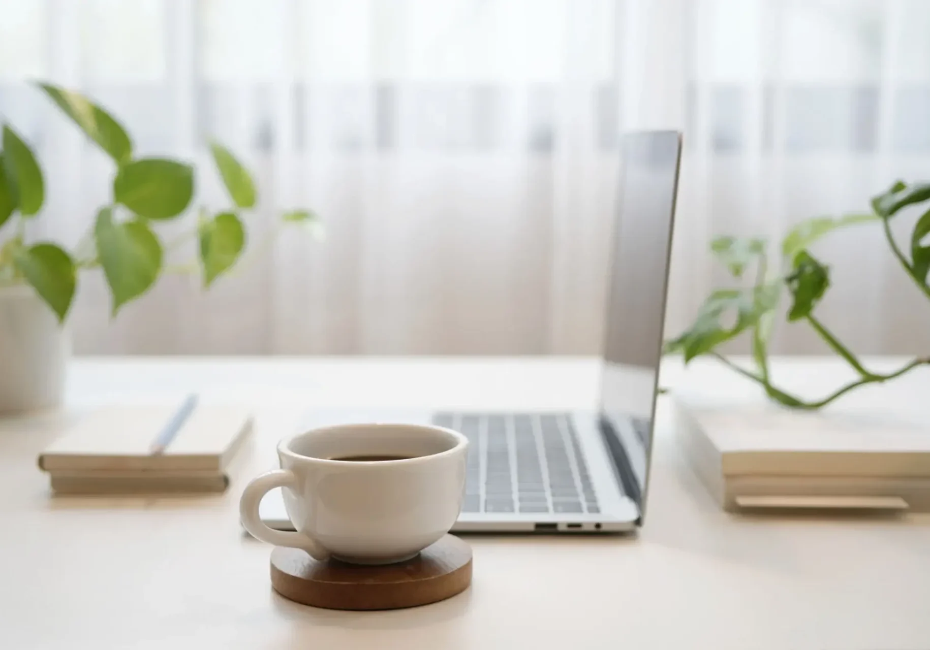 A coffee cup next to an open laptop on a bright desk.